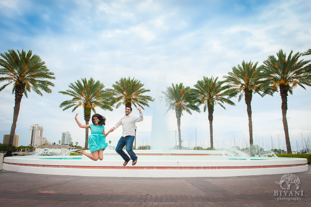 Engaged Indian Couple jumping with joy in front of palm trees and a fountain, across the street from the Dali Museum in Tampa, Florida