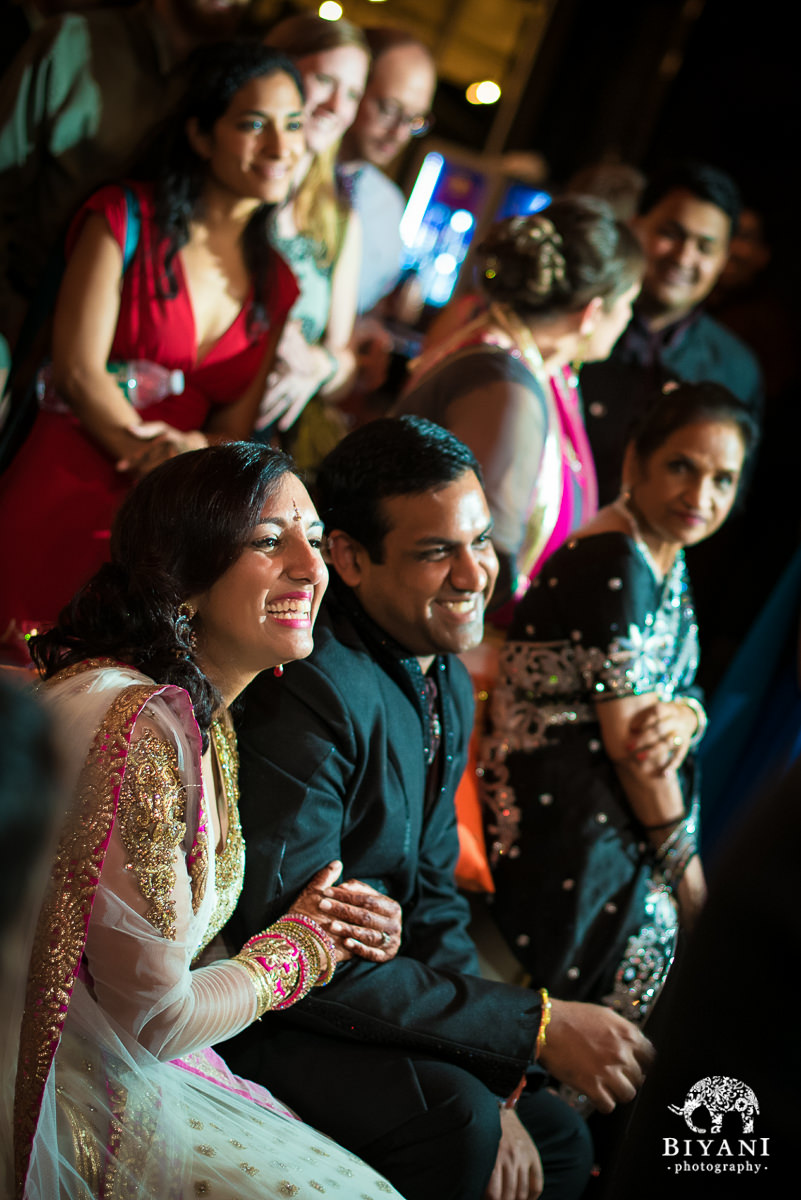 Couple smiling and laughing during Sangeet toasts from friends