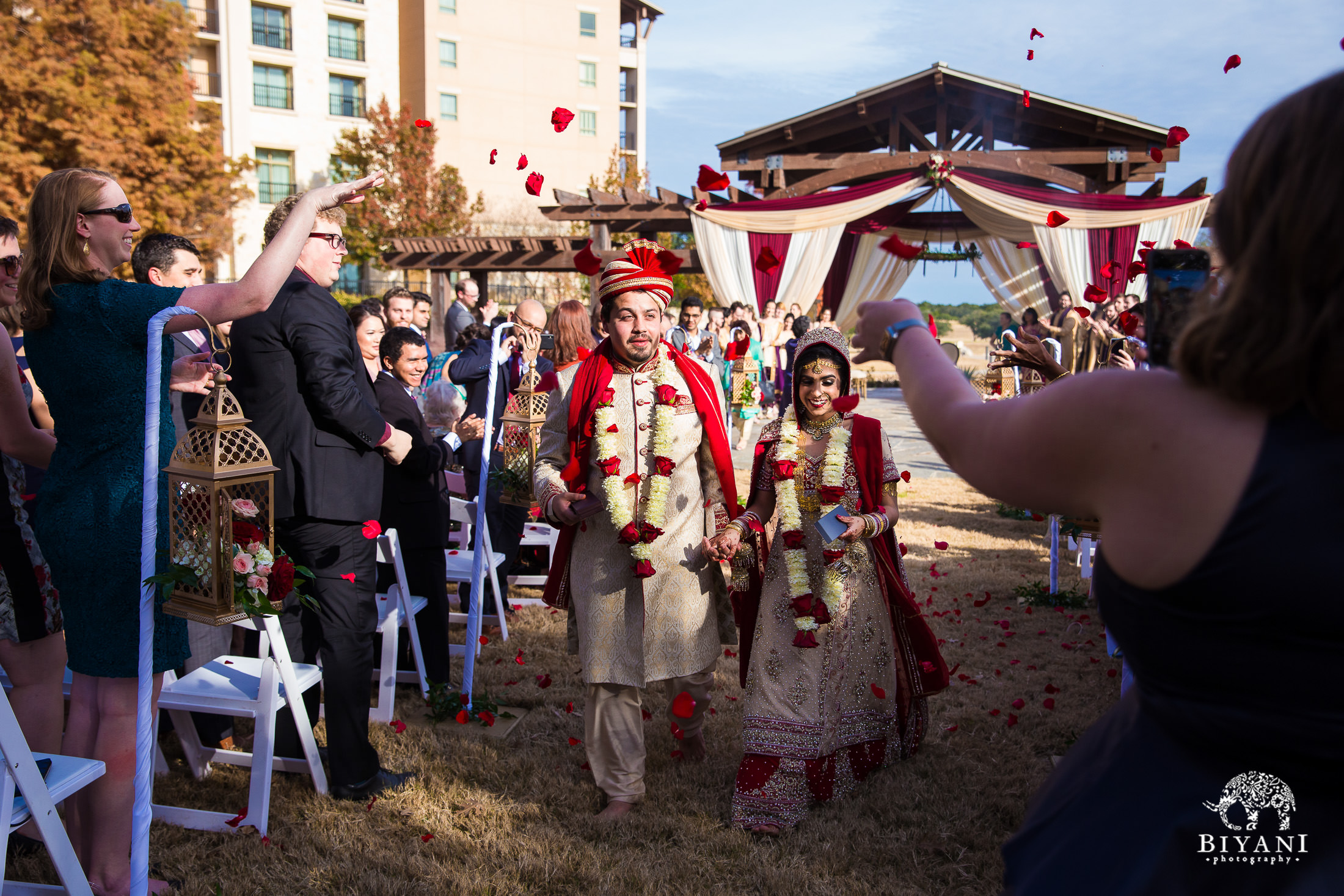 Indian Fusion bride and groom walking down the aisle together after Indian wedding ceremony  while guests throw rose petals on them