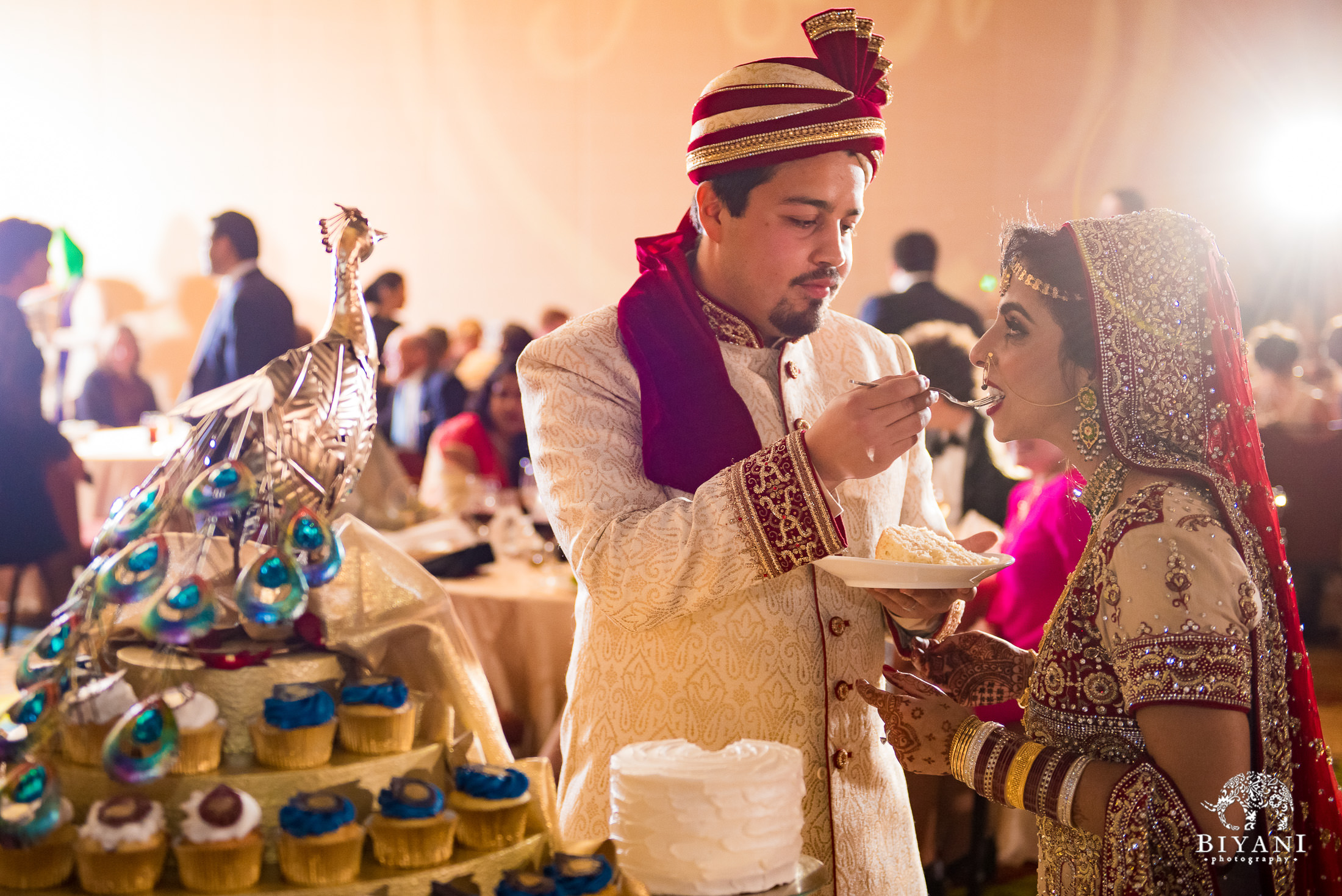 Groom feeds bride cake during Indian Fusion wedding reception party