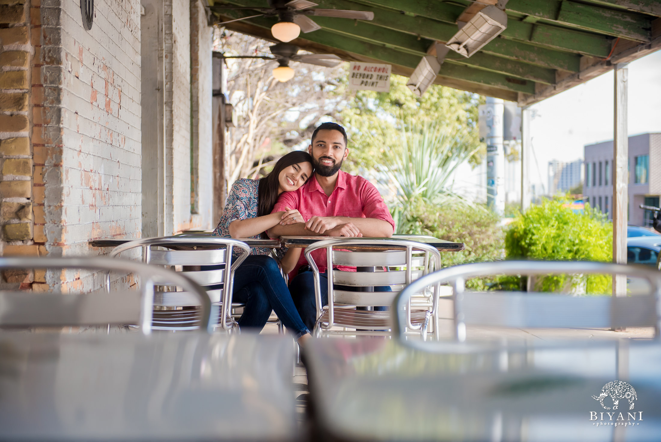 Indian couple sitting down at a restaurant table during their engagement photo shoot in South Congress Austin, Tx. on a sunny day