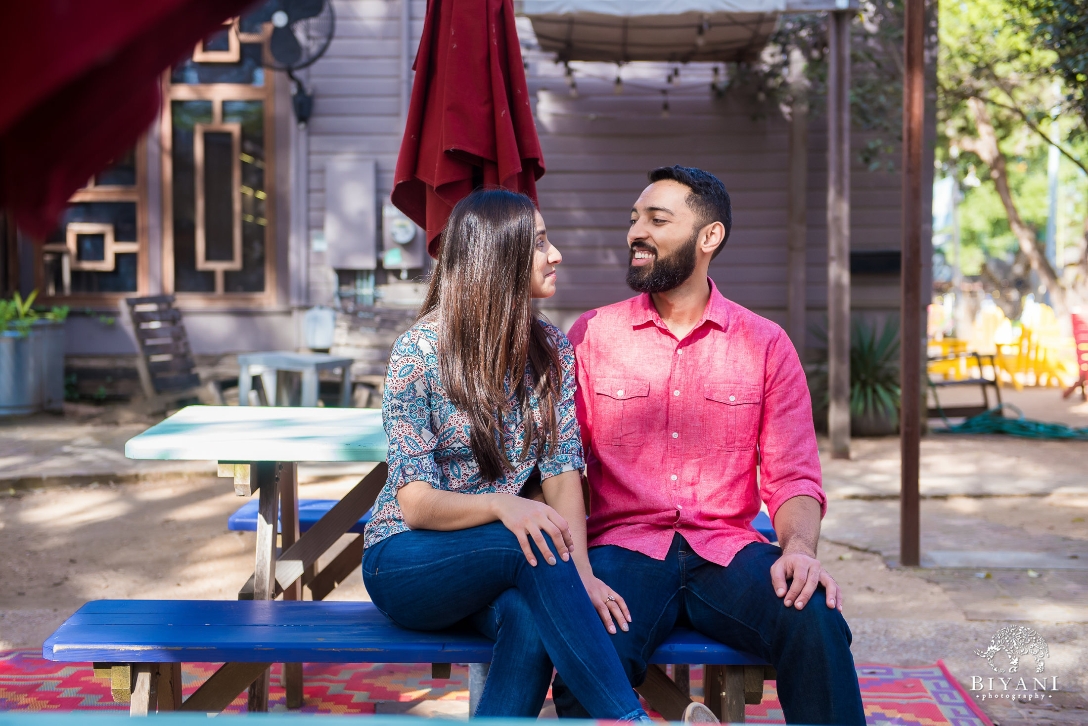 Indian couple sitting down on a picnic bench under a canopy during their engagement photo shoot in South Congress Austin, Tx. on a sunny day