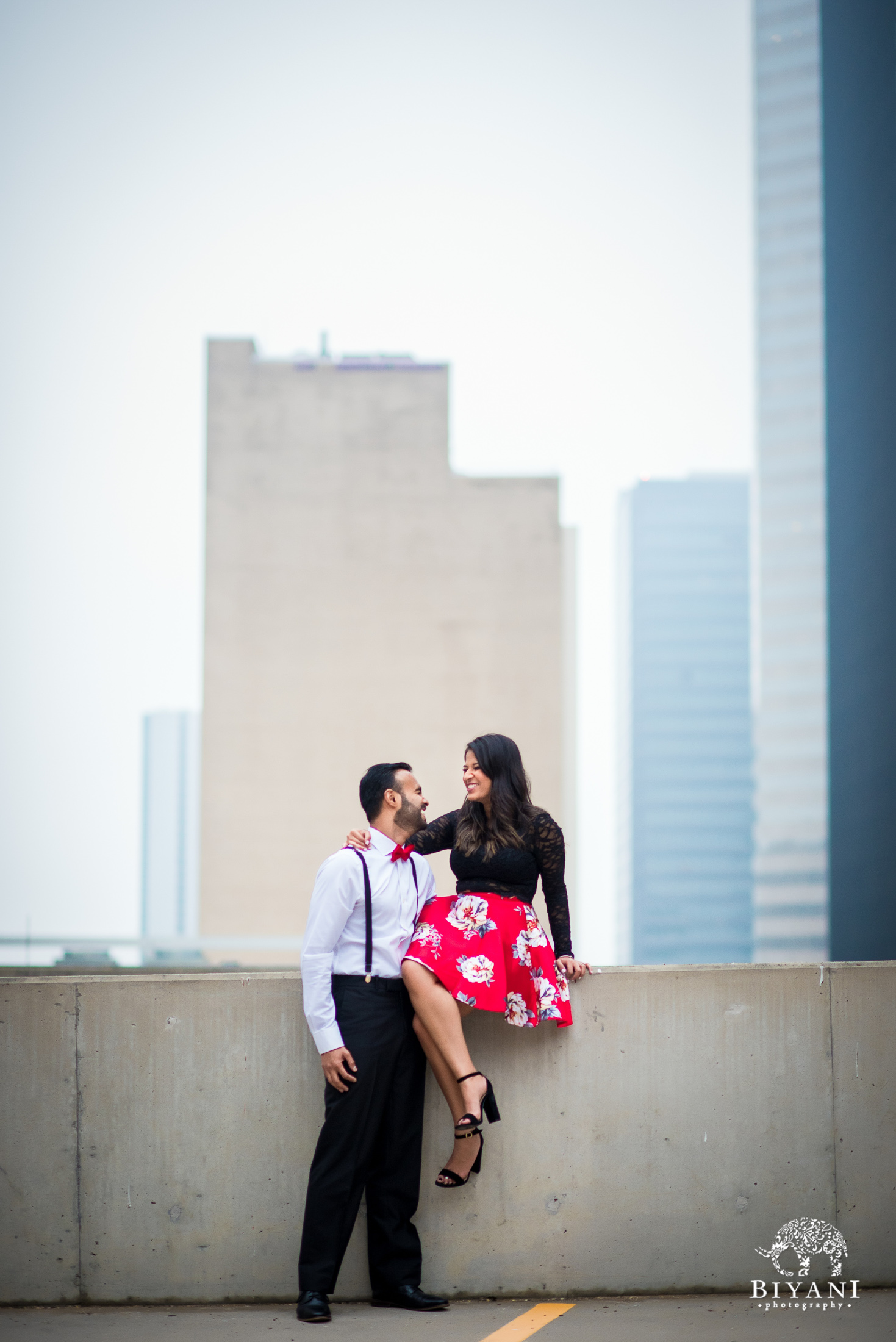Sri Lankan couple during an engagement photo shoot sitting on the ledge overlooking Houston city skyline