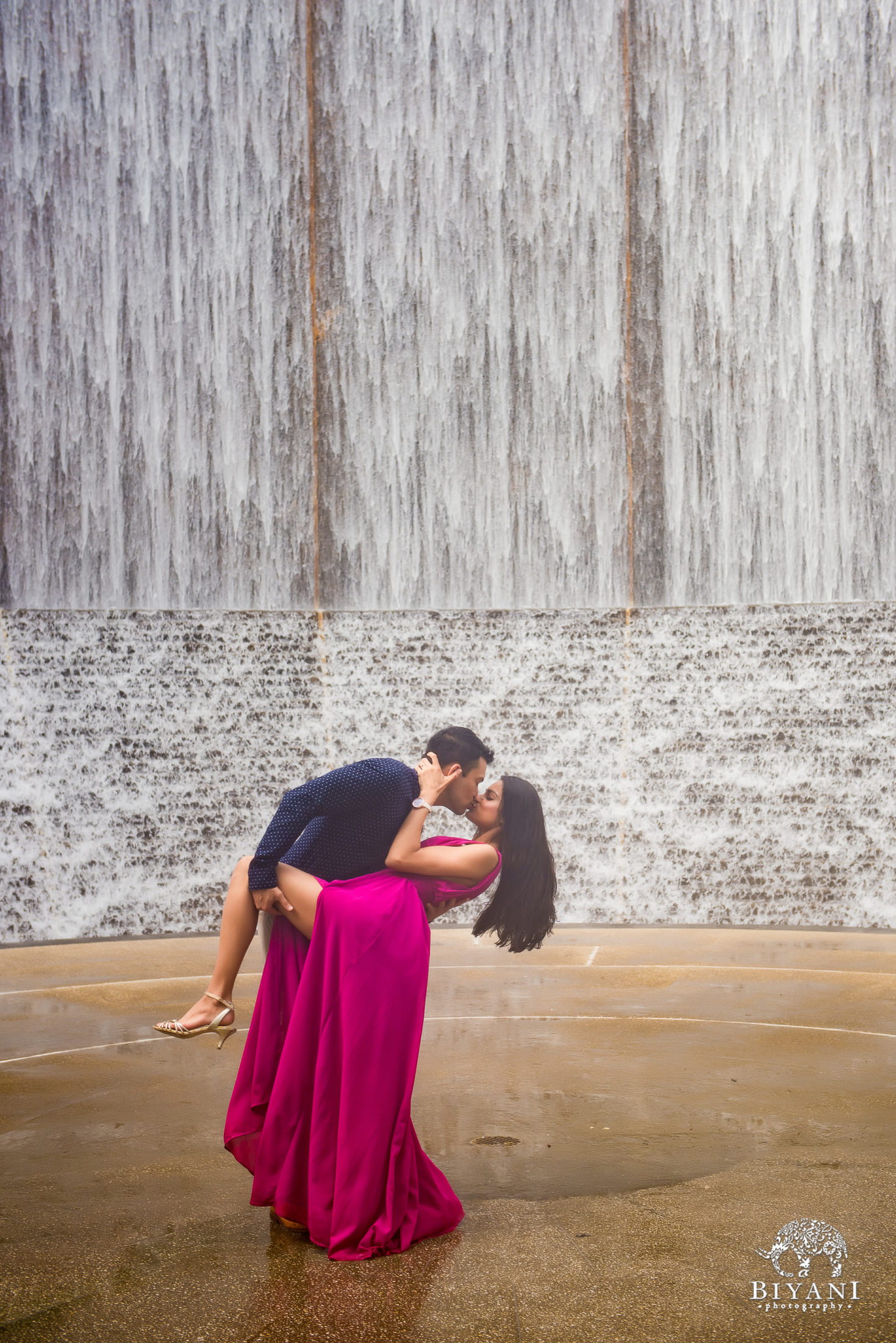 couple posing with leg up at water wall near Houston Galleria