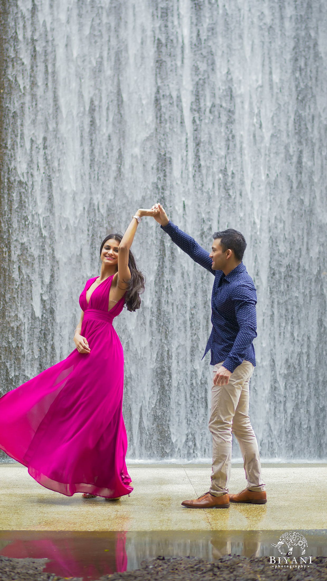 engagement couple twirling in front of water wall at the Houston Galleria