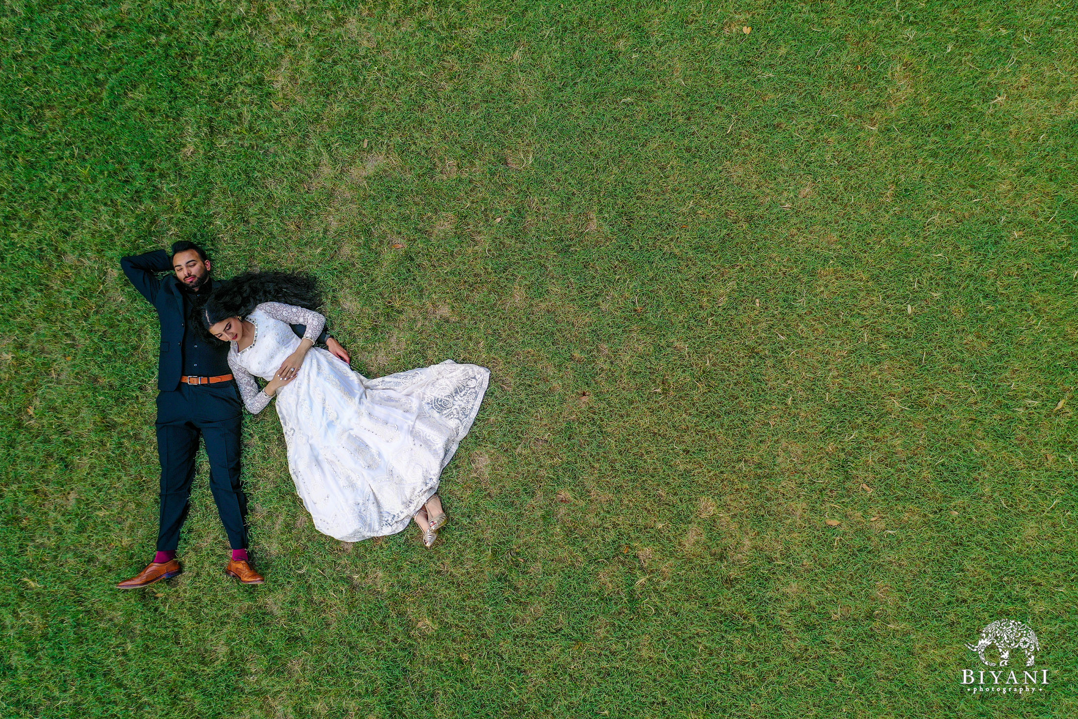 drone photo of bride laying on groom's chest in the grass