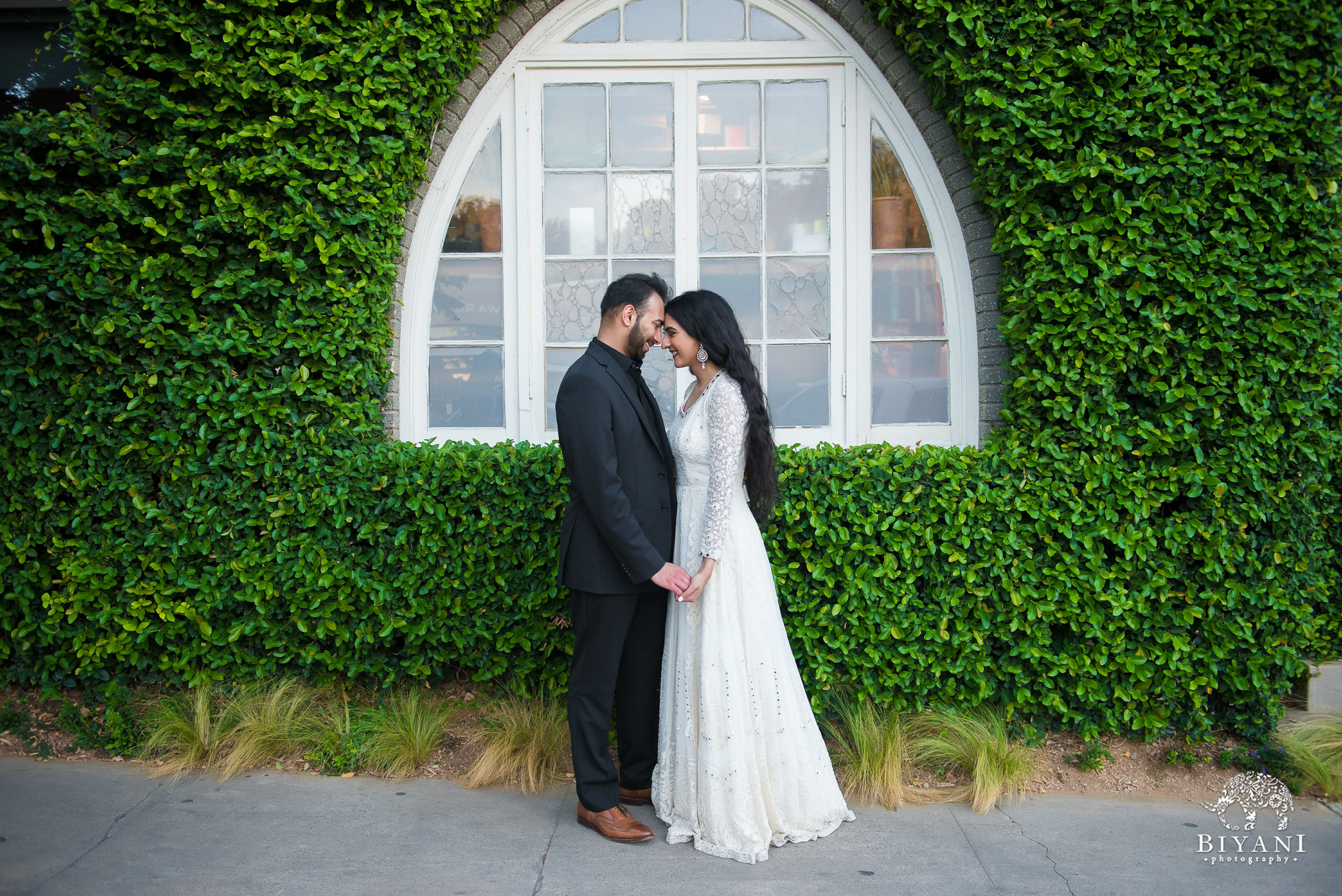 couple touching foreheads together in front of a vintage window with ivy growing around it