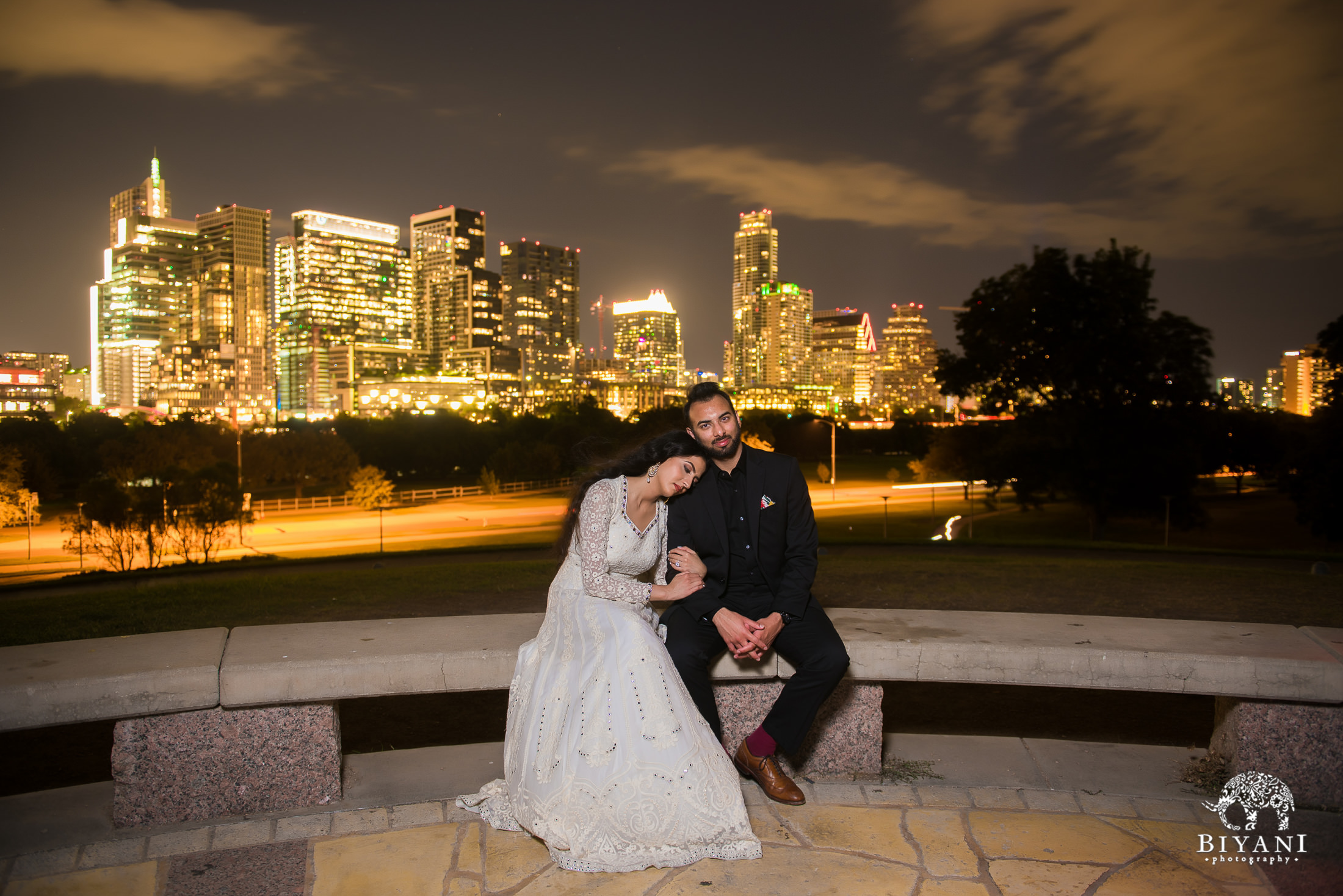 couple sitting on bench together in front of Austin city skyline during night