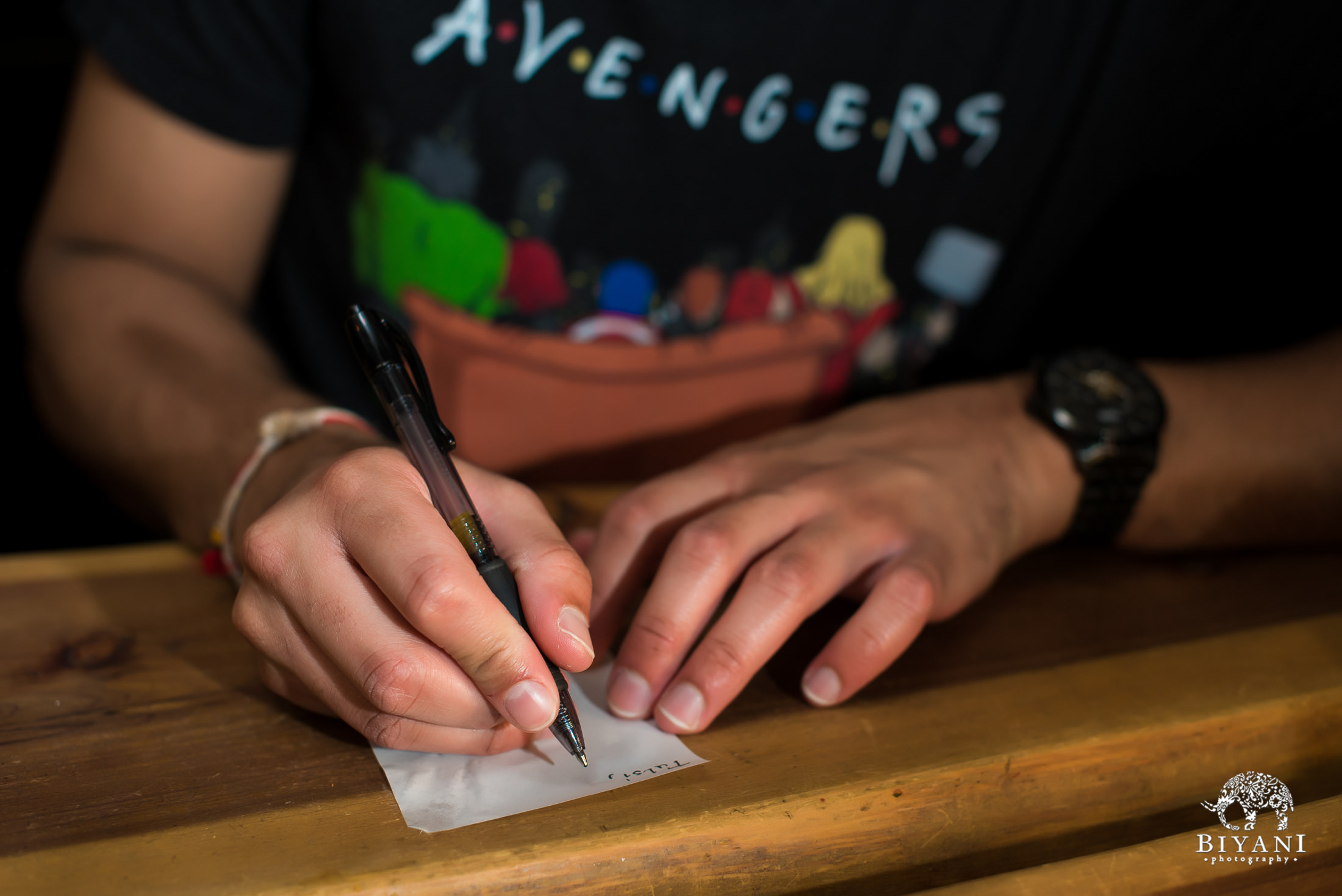 Groom writing secret love letter for bride at coffee shop wearing an Avengers t-shirt