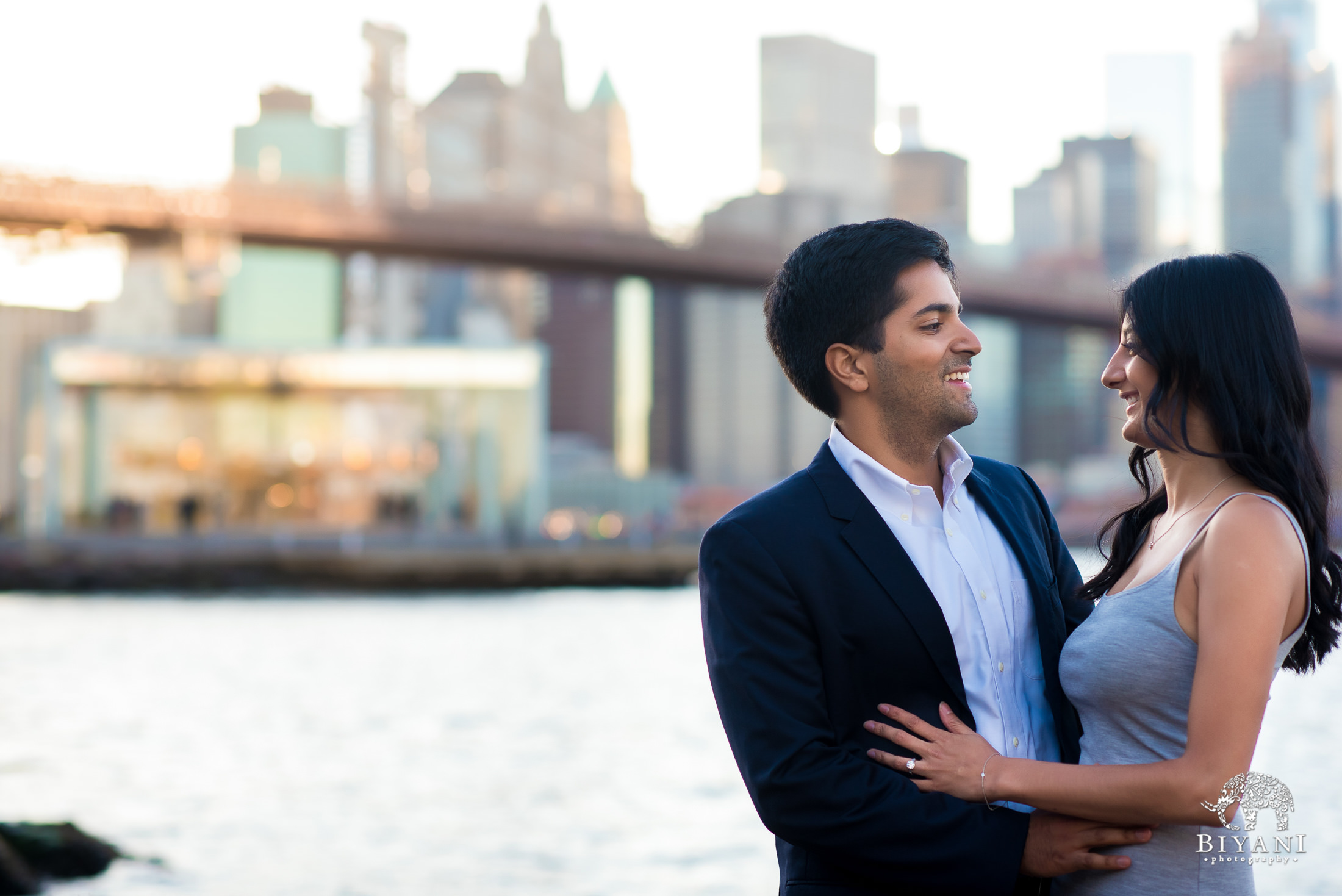 engagement shoot in front of Brooklyn Bridge in New York City with couple looking at each other